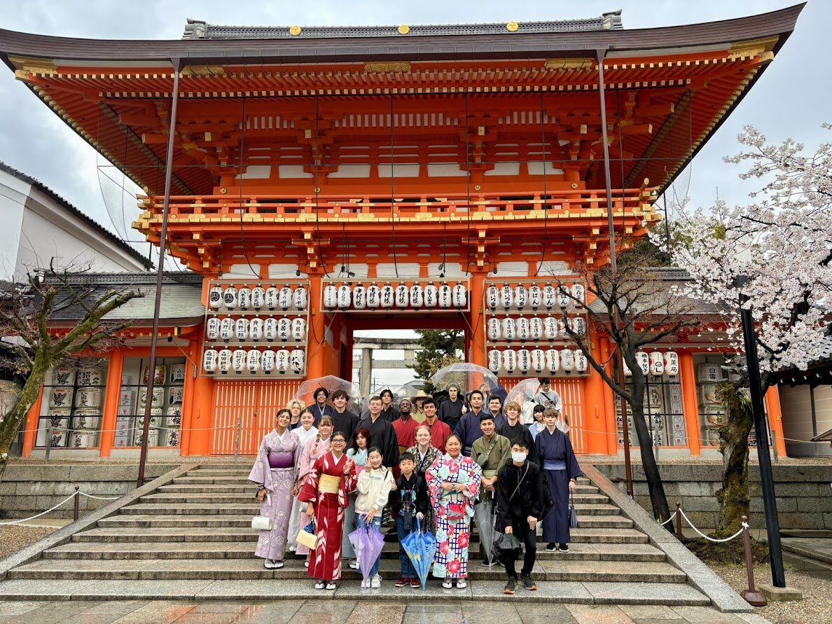 Students in kimono at a shrine gate during cherry blossom season